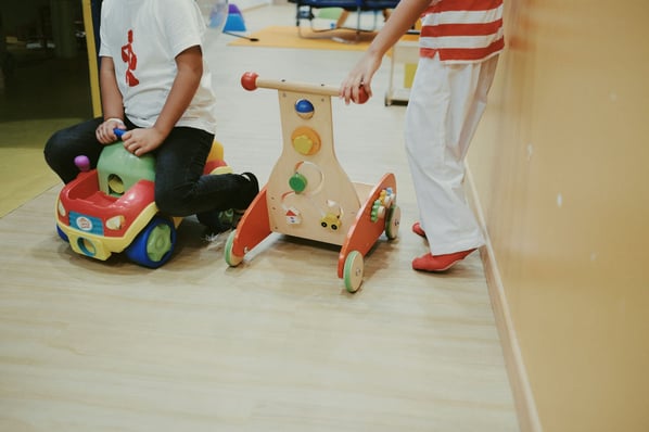 Two children playing with car and tricycle toys in the classroom.
