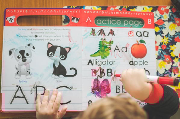 A young child tracing letters in an activity book, demonstrating the emergent writing measure.