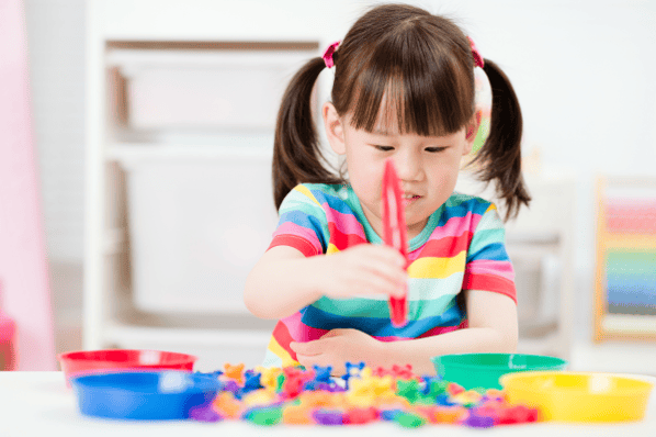Toddler in a striped shirt sitting at a desk practicing her fine motor skills.