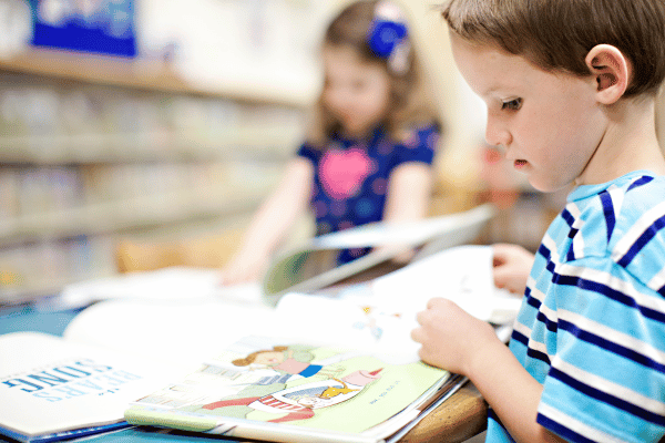 Young boy reading a picture book at a table.